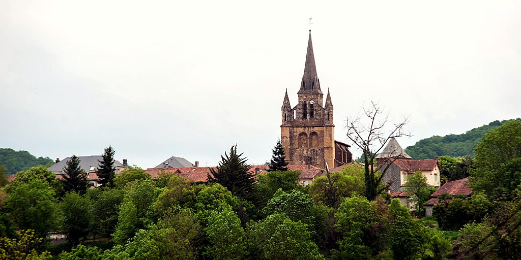 Le clocher de Galan dépasse des arbres et des toits du village, devant les collines.