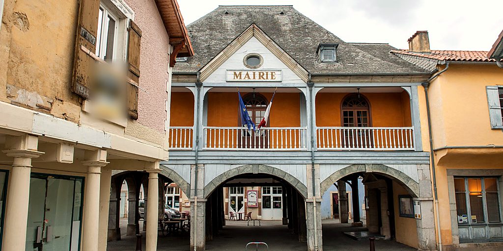 La mairie de Galan, avec son balcon et ses drapeaux, au-dessus des arcades de la halle.