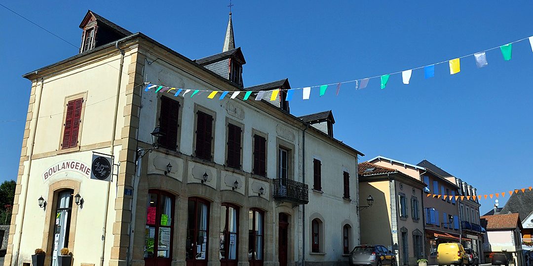 Façade de la boulangerie et des maisons de la place, décorées de fanions colorés.