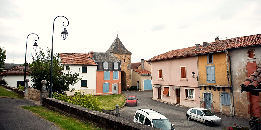 Rue bordée de maisons aux façades colorées, menant à la tour-porte sud et à son toit pointu.